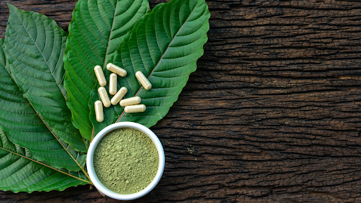 A kratom leaf sprinkled with powder, highlighting its products in powder and capsule form